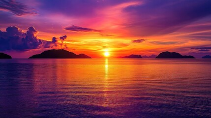 Naklejka premium The sun setting behind distant islands on a calm sea, with the colorful evening sky filled with shades of purple, orange, and red, creating a peaceful seaside moment.