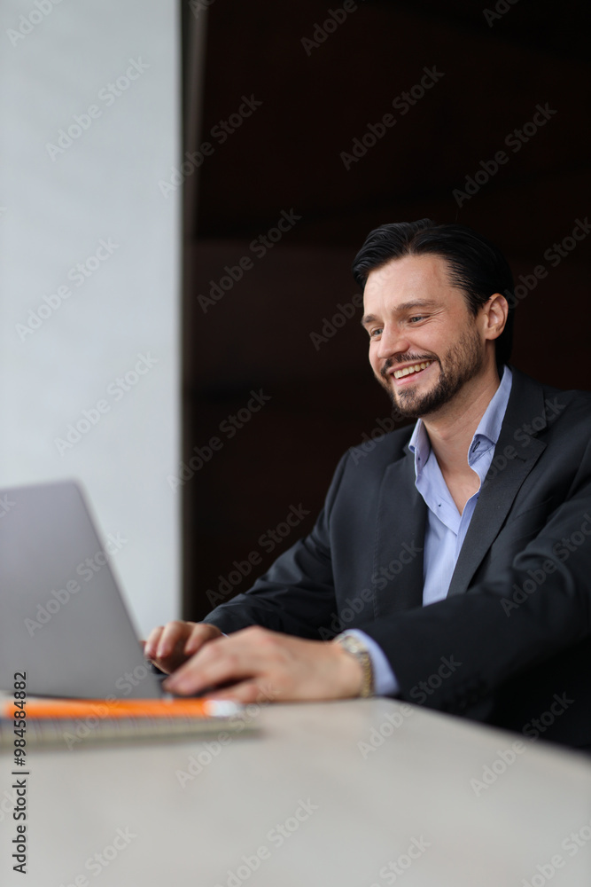 Aufkleber a man is sitting at a desk with a laptop in front of him. he is smiling and he is enjoying himself
