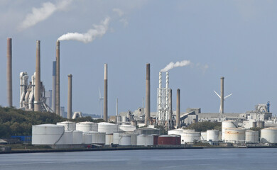 huge cement factory with very tall chimneys puffing out white smoke and seashore during production