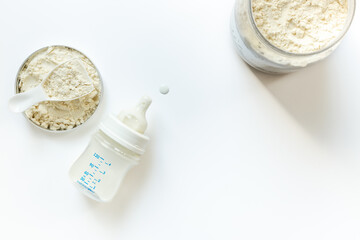 Jar of powdered milk for baby food with bottle of milk and spoon, top view