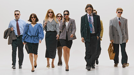 Business professionals, all stylishly dressed in formalwear and sunglasses, walking with purpose against white studio background. Concept of corporate culture, business and style, leadership. Ad