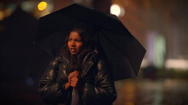 A woman holding an umbrella stands in a rainy cityscape, capturing the essence of urban life