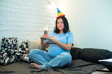 pregnant 42 year old woman with birthday cake and candle on bed at home. pregnancy after 40,...