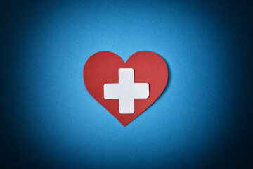 Organ donation with white paper health cross on red heart