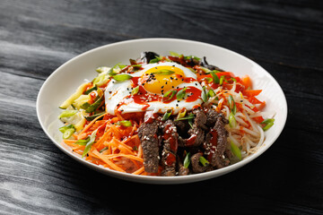 Traditional Korean dish Bibimbap with rice, vegetables beef and egg in a white plate