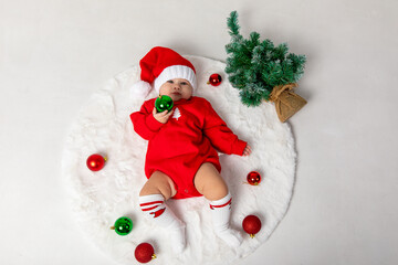 Top view Christmas portrait of cute little newborn baby girl, wearing red Santa hat with Christmas balls on a white background. Christmas and New Year concept.