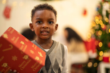 A young child excitedly holding a Christmas gift box, surrounded by festive decorations and...