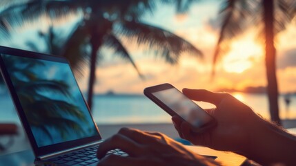 A person working on a laptop while using a smartphone against a beautiful sunset by the beach with palm trees in the background