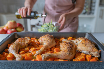 Roasted chicken legs with sweet potatoes on a baking tray fresh and homemade prepared by a woman in the kitchen
