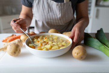 Homemade fresh cooked vegetarian potato soup with white beans served by a woman with apron in the kitchen