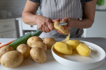 Woman ist peeling with a knife in her hands fresh and raw potatoes