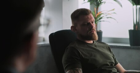 Unhappy military man with post traumatic stress disorder sits in chair, shares feelings and communicates with psychotherapist or psychologist on rehabilitation therapy session. PTSD. Over the shoulder