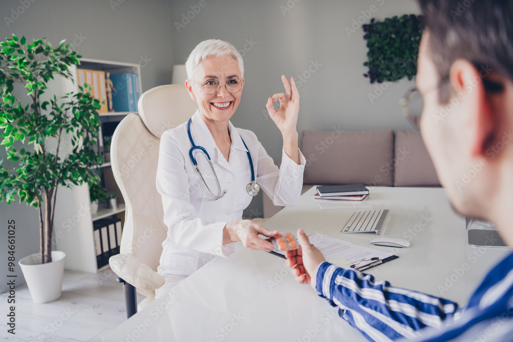 Sticker Portrait of aged woman professional doctor give patient pills show okey symbol wear white coat workplace office indoors