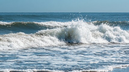 A serene view of ocean waves crashing on a shore under clear blue skies.