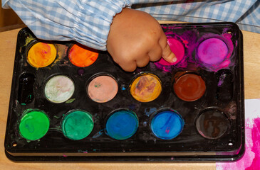 a child's finger picking up finger paint from a watercolor palette