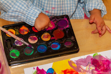 a child's finger picking up finger paint from a watercolor palette