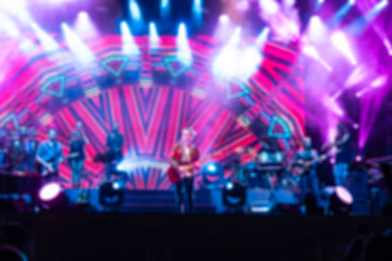 Fototapeta premium Blurred background rock concert with light background, concert in hall at night. people enjoying music performance in hall. musicians on the stage and spotlights with colored rays. concert and crowd.