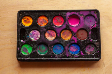 Palette of watercolor paints on a wooden background. Top view.
