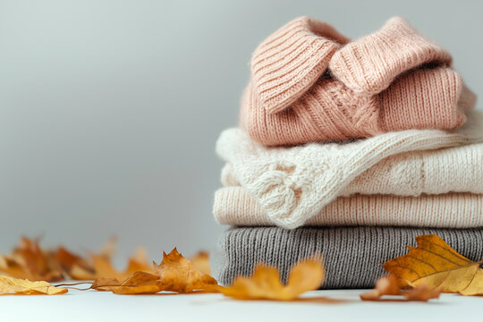 Stack of colorful knitted sweaters. Folded soft sweaters with autumn leaves on neutral background with copy space. Hello Autumn concept. Autumn clothes, fashion and sale, knitting
