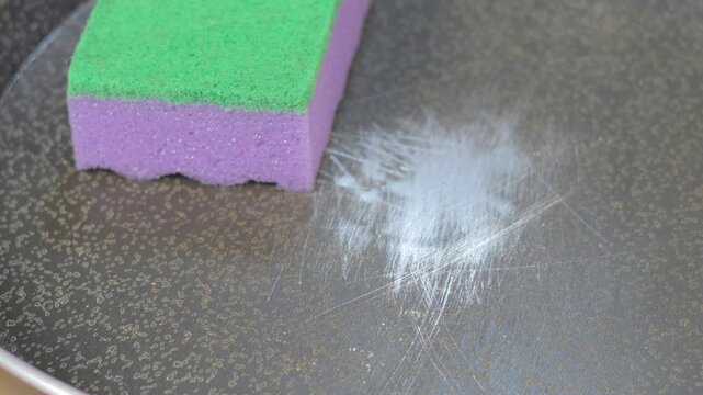 Close up view of a sponge for washing dishes in scratched Teflon pan. Pan peeling off.