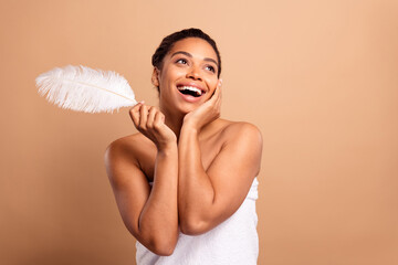 Photo of gorgeous cheerful woman look empty space hold soft feather naked shoulders isolated on...