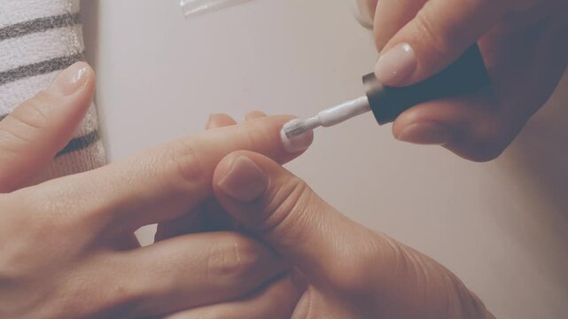 Manicurist painting her client's nails. Professional manicurist applying white nail polish to young girl's nails.