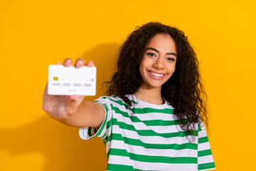 Portrait of nice young girl hold debit card wear striped t-shirt isolated on yellow color background