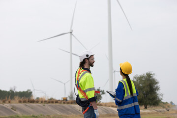 Male and female engineer at windmill field farm, wearing safety uniform and working and inspecting quality of wind turbines