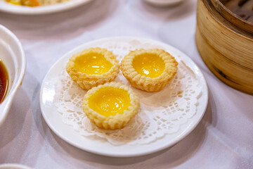 A plate of three golden Chinese egg tarts arranged on a doily, highlighting their rich custard centers and buttery, flaky crusts, served at a dim sum meal.