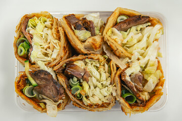 Close-up of Taiwanese beef rolls with crispy outer layer, fresh lettuce, green onions, and tender beef filling, arranged neatly in a plastic container