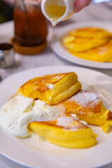 ight and fluffy souffle pancakes being drizzled with syrup, served with whipped cream on a white plate, capturing the soft texture and golden color