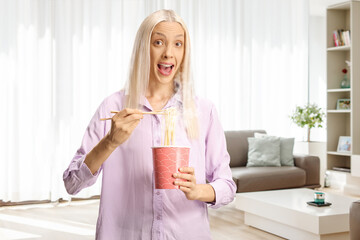 Excited young woman eating noodles from a takeaway box