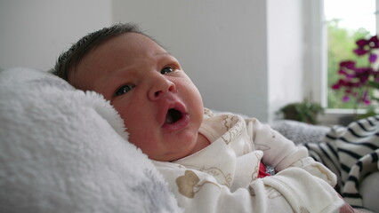 Close-up of baby resting on soft blanket, gazing calmly, natural light from a nearby window...