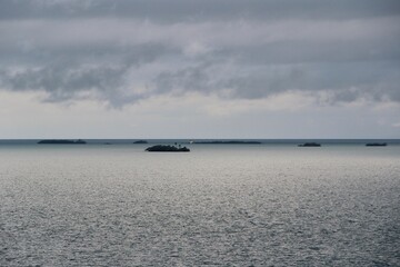 Serene view of small islands dotting the calm turquoise sea under moody, cloud-filled skies. A...