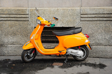 Vibrant orange scooter parked against stone wall on city street