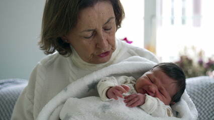 Grandmother holding newborn baby, gazing down lovingly, capturing a moment of warmth and connection...