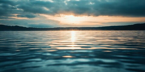 Obraz premium Sunset casting a golden glow over a calm lake, its reflection creating ripples that add an element of movement to the serene scene.