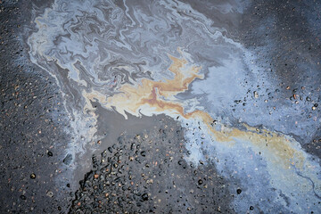 Close-up of an iridescent oil or gasoline spill on a wet asphalt, viewed from above. Bold...