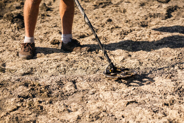 A man with a metal detector looking for antique valuables in the ground.