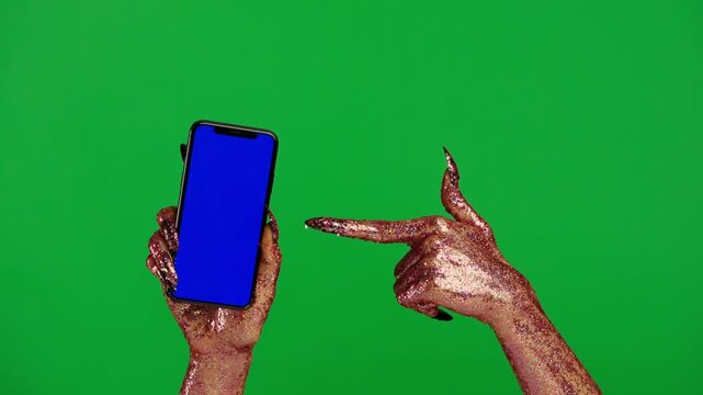 Creepy halloween monster human hand in glitter slime with nails holding pointing at smartphone, isolated on chroma key green screen background, workspace mockup.