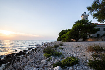 Beautiful sunset in a landscape on a rocky coast with a striking lighthouse and pine forest. View...