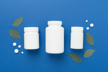 Bottle with pills and green leaves on color background, top view