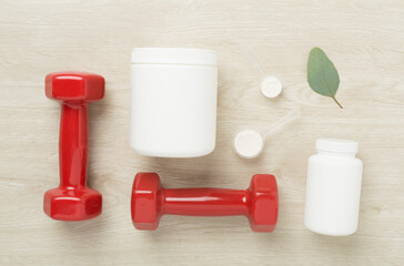 Jars with protein powder and dumbbells on wooden background, top view. Sports nutrition concept