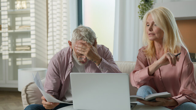 Upset retired mature Caucasian woman man couple senior elderly male female arguing worrying laptop problem online banking loss error wife husband family quarrel losing money bankruptcy conflict home