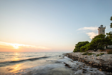 Beautiful sunset in a landscape on a rocky coast with a striking lighthouse and pine forest. View...