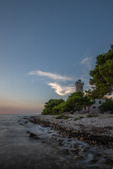 Beautiful sunset in a landscape on a rocky coast with a striking lighthouse and pine forest. View over the coast to the building, on the Mediterranean, Vir, Dalmazien, Croatia, Adriatic