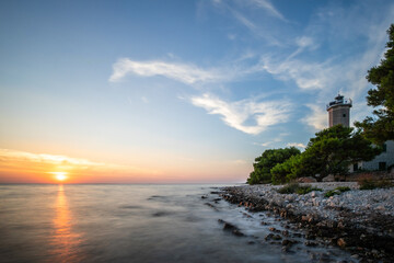 Beautiful sunset in a landscape on a rocky coast with a striking lighthouse and pine forest. View...