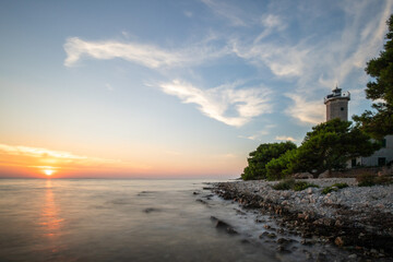 Beautiful sunset in a landscape on a rocky coast with a striking lighthouse and pine forest. View...