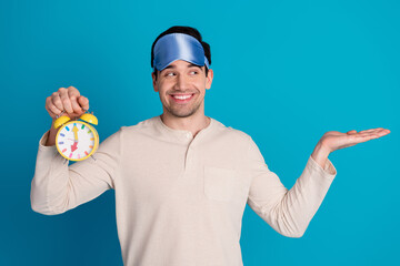 Photo of nice young man hold empty space alarm wear pajama isolated on blue color background