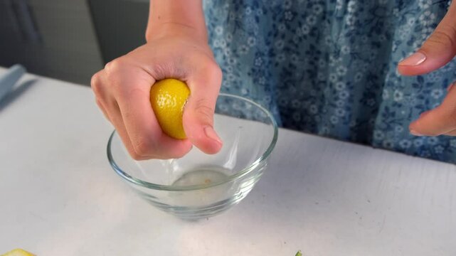 Woman hands squeeze lemon juice into glass bowl cooking on kitchen at home. Preparing ingredient for dish or beverage. Recipe cuisine professional culinary. Prepare fruit dessert homemade drink.